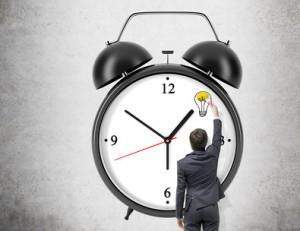 Young businessman painting with a brush on a concrete wall the image of a huge alarm clock. Back view. Concept of time.